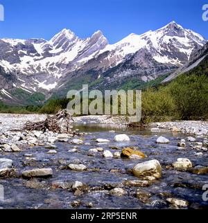 Ein ruhiger Bergfluss in den Pyrenäen, in der Nähe des Dorfes Bielsa, mit großen Steinen, im Hintergrund schöner Blick auf hohe Berge mit Schnee bedeckt Stockfoto