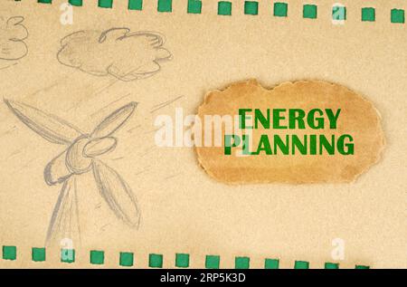 Ein Windgenerator und Wolken sind auf Karton mit grünen Löchern gezeichnet, daneben liegt ein Karton mit der Aufschrift - Energy Planning. Ökologisch Co Stockfoto