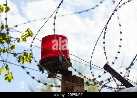 Geschützter Bereich. Ein Zaun mit Stacheldraht und einem roten Blinker vor einem Himmel mit Wolken. Stockfoto