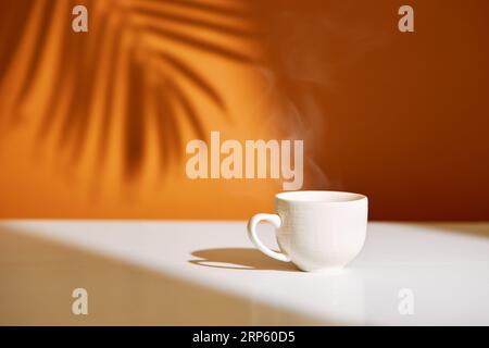 Nahaufnahme der Kaffeetasse auf dem Tisch bei direkter Sonneneinstrahlung. Morgenkaffee mit Dampf in weißer Tasse. Stockfoto