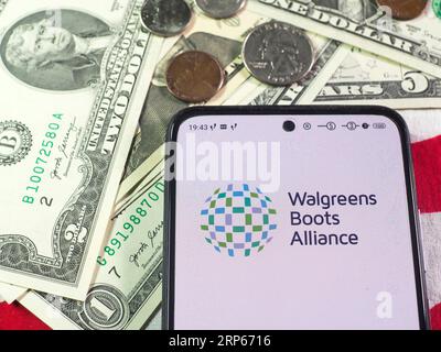 In dieser Abbildung wird das Logo von Walgreens Boots Alliance, Inc. Auf einem Smartphone und US-Banknoten und -Münzen im Hintergrund angezeigt. Stockfoto