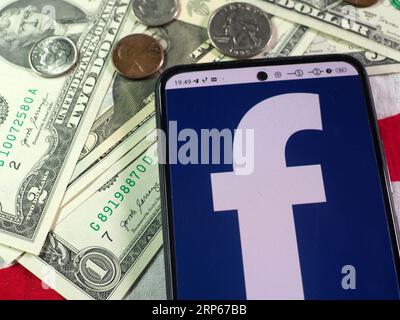 In dieser Abbildung wird das Facebook-Logo auf einem Smartphone und US-Banknoten und -Münzen im Hintergrund angezeigt. Stockfoto