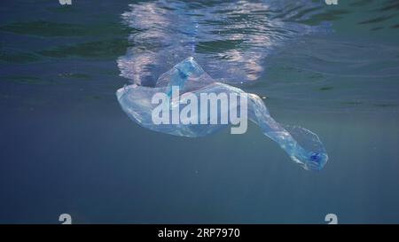 Blauer Einweg-Plastikbeutel schwimmt unter der Oberfläche in blauem Wasser. Plastiktüte, die ins Meer geworfen wurde, treibt morgens unter blauem Wasser, Rot Stockfoto