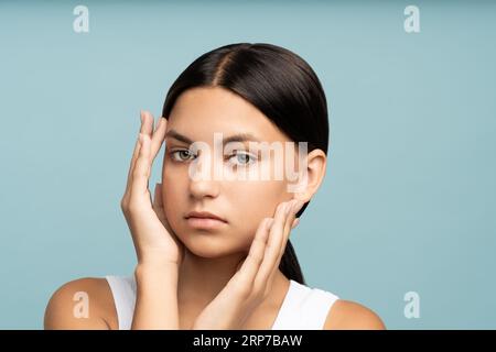 Nahaufnahme eines glücklichen Mädchengesichts mit natürlichem gekämmtem Haar, das gut gepflegte, reine, perfekte Haut berührt Stockfoto