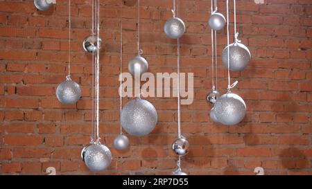Silberne Weihnachtskugeln auf dem Hintergrund einer Mauer aus rotem Ziegelloft Stockfoto