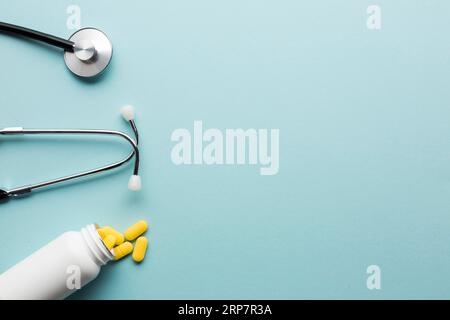 Gelbe Tabletten, die aus der weißen Flasche in der Nähe der blauen Oberfläche des Stethoskops austreten Stockfoto