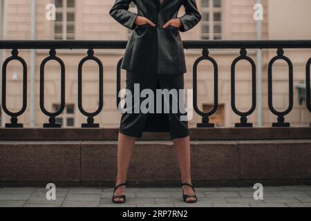 Modische Details eines langen Rockes aus schwarzem Leder und einer schicken Jacke. Frau posiert in der Stadt. Trendiges Stoffkonzept im Streetstyle Stockfoto