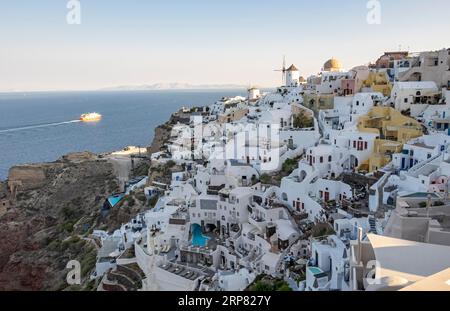 Häuser an den Klippen, Villen und Windmühle im Dorf Oia, Ia, vom Schloss Kasteli, Santorin, Griechenland aus gesehen Stockfoto