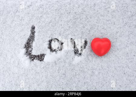 Das Wort Liebe, das im Schnee geschrieben wurde, mit einer roten Herzfigur anstelle des Buchstabens E Stockfoto