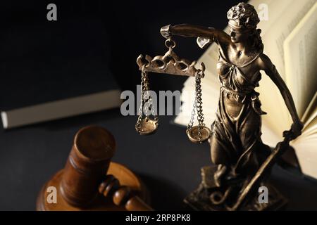 Symbol der gerechten Behandlung nach dem Gesetz. Statue von Lady Justice in der Nähe des Nabels und offenes Buch auf schwarzem Tisch Stockfoto