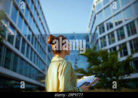 Hinter einer Arbeiterin in der Nähe eines Business Centers in einer grünen Bluse mit Dokumenten auf dem Smartphone. Stockfoto