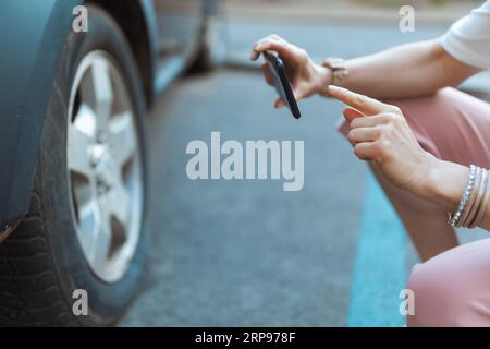 Autounfall. Nahaufnahme einer Reisenden Frau in der Stadt mit Smartphone, die ein Foto in der Nähe eines Autos mit einem Platten Reifen macht. Stockfoto