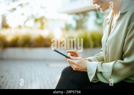 Nahaufnahme einer glücklichen weiblichen Mitarbeiterin im Geschäftsviertel in grüner Bluse und Brille mit Smartphone. Stockfoto