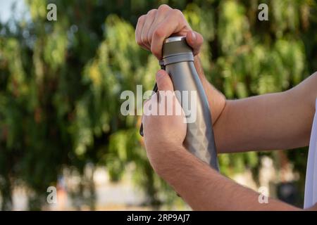 Nahaufnahme der Hände eines jungen Kaukasiers, der eine Metallwasserflasche hält. Leerzeichen links kopieren Stockfoto