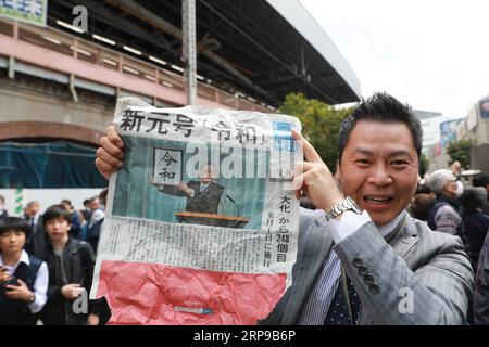 (190401) -- TOKIO, 1. April 2019 (Xinhua) -- Ein Mann hält eine Zeitung über Japans Chef-Kabinettssekretär Yoshihide Suga, der ein gerahmtes Bild von Reiwa, dem Namen der neuen Ära Japans, während einer Pressekonferenz in Tokio, Japan, am 1. April 2019 in der Höhe hält. Die japanische Regierung gab am Montag bekannt, dass Reiwa der Name der neuen Ära Japans sein wird, die am 1. Mai beginnen wird, als Kronprinz Naruhito den Chrysanthemen-Thron als Nachfolger seines Vaters Kaiser Akihito bestiegen wird. Der Name der neuen Ära, der aus zwei chinesischen Schriftzeichen besteht, die grob in Ordnung oder Verheißung und Frieden oder Harmonie übersetzt werden, ist abgeleitet Stockfoto