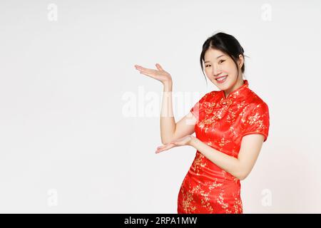 Glückliches chinesisches Neujahr. Asiatische Frau trägt traditionelles Cheongsam Qipao Kleid mit Geste der Einführung isoliert auf weißem Hintergrund. Stockfoto