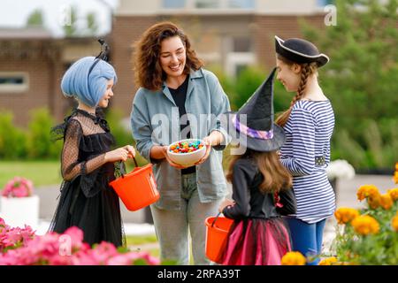 Glückliche Leute feiern Halloween. Erwachsene behandelt Kinder im Freien mit Süßigkeiten. Stockfoto