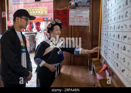 (190424) -- LIJIANG, 24. April 2019 (Xinhua) -- Ein Einheimischer stellt einem Touristen in der antiken Stadt Lijiang in der südwestlichen chinesischen Provinz Yunnan am 22. April 2019 Hieroglyphen vor. Nach Angaben der örtlichen Behörden begann der Tourismus zu erhitzen, als Anfang 2019 ein schnellerer Zugverkehr zwischen Lijiang und der Provinzhauptstadt Kunming eingeführt wurde. In der ersten Saison begrüßte Lijiang 12,325 Millionen Ankömmlinge und erzielte einen Gesamtumsatz von 25,637 Milliarden Yuan, was einem Anstieg um 21,5 Prozent bzw. 15,13 Prozent gegenüber dem Vorjahr entspricht. (Xinhua/Hu Chao) CHINA-YUNNAN-LIJIANG-TOURISM (CN) PUBLICATIONxNOTxINx Stockfoto