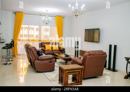 Ein modernes Wohnzimmer mit hellgelben Fenstervorhängen und einem Fernseher an der Wand Stockfoto