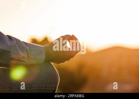 Nahaufnahme der männlichen Hand in Meditationsposition bei warmem Sonnenuntergang, Meditation und Achtsamkeitskonzept Stockfoto