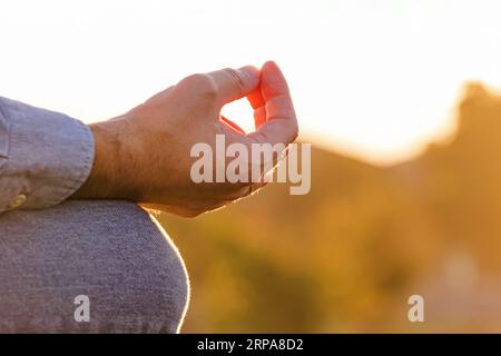 Nahaufnahme der männlichen Hand in Meditationsposition bei warmem Sonnenuntergang mit verschwommenem Hintergrund Stockfoto