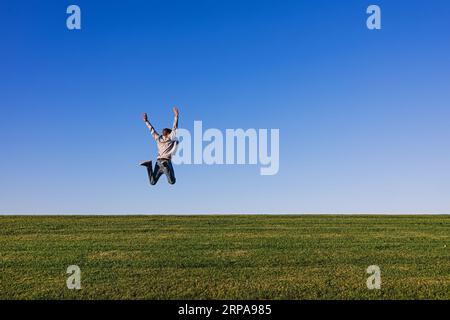 Glücklicher Mann, der frische Luft und Natur genießt und am Horizont auf dem grünen Gras springt Stockfoto