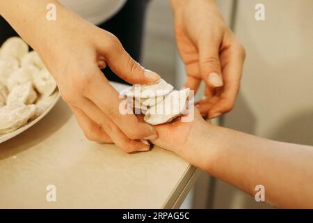 Eine Frau legt gekochte Knödel auf die Hand des Kindes. Nahaufnahme. Stockfoto