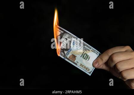 Menschliche Hand mit einer brennenden 100-Dollar-Rechnung. Konzept der Inflation, der Abnahme des Erwerbs von Fremdwährungen und der Devisenabwicklung. Stockfoto