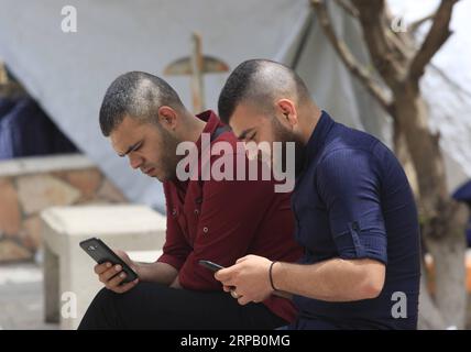 (190523) -- GAZA, 23. Mai 2019 -- palästinensische junge Männer Amin Abed (L) und Mohammed al-Bourno benutzen ihre Telefone, um an einer Online-Kampagne in Gaza-Stadt zu arbeiten, 22. Mai 2019. Eine Gruppe palästinensischer Jugendlicher im Gazastreifen hat eine Online-Kampagne gestartet, um die israelische Erzählung zu widerlegen. ZUM MITNEHMEN: Palästinensische Jugendliche starten Kampagne, um israelische Erzählungen zu widerlegen Stringer) MIDEAST-GAZA-ONLINE-KAMPAGNE zhaoyue PUBLICATIONxNOTxINxCHN Stockfoto