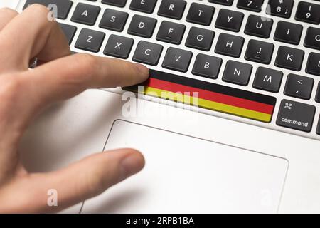 Online-Internationales Geschäftskonzept: Computerschlüssel mit deutscher Flagge darauf. Männliche Hand drückt Computerschlüssel mit deutscher Flagge Stockfoto