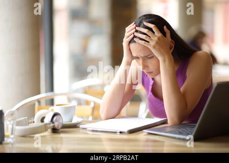 Trauriger Schüler, der versucht, Notizen zu lesen und sich auf einer Bar-Terrasse zu beschweren Stockfoto