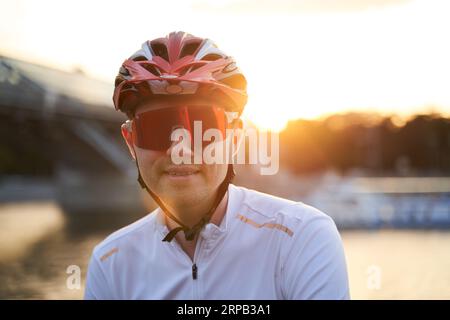 Der Mann trägt einen Schutzhelm, eine Sonnenbrille und Sportkleidung während der abendlichen Fahrt in der Stadt. Nahaufnahme Stockfoto