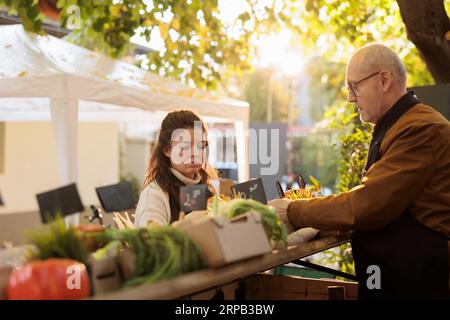 Familienpaare oder Biobauern, die auf ihre ersten Kunden warten, während sie auf dem Bauernmarkt arbeiten. Händler, die Produkte vorbereiten, verkaufen frisches Obst und Gemüse aus eigener Produktion Stockfoto