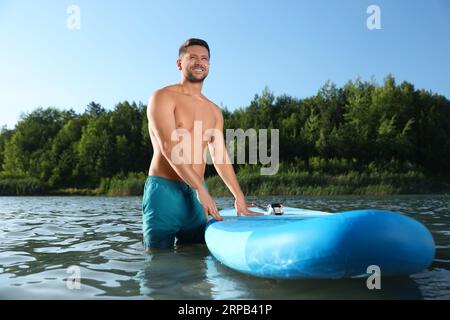 Ein Mann steht am sonnigen Tag neben dem SUP-Brett im Flusswasser Stockfoto