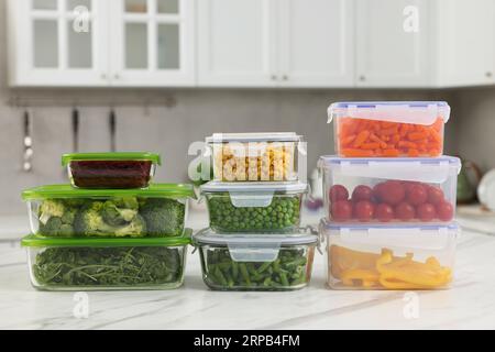 Glas- und Kunststoffbehälter mit verschiedenen frischen Produkten auf einem weißen Marmortisch in der Küche. Lebensmittelaufbewahrung Stockfoto