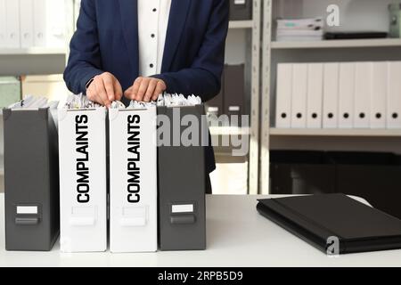 Frau durchsucht Dokumente im Ordner mit Reklamationsaufkleber im Büro, Nahaufnahme Stockfoto