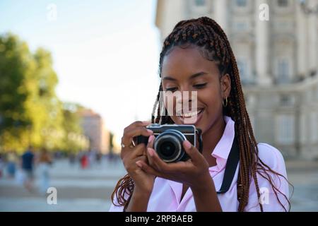 Schwarze Touristenfrau lächelt und macht Fotos mit einer Kamera während der Besichtigungstour in Madrid, Spanien. Stockfoto