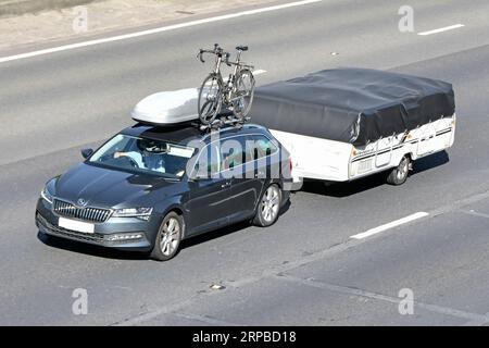 Schwarzes fünftüriges Fließheck-Auto mit zusammenklappbarem Campinganhänger, ausgestattet mit Dachgepäckkasten und Fahrradträger, fahren auf der M25-Autobahn England Großbritannien Stockfoto