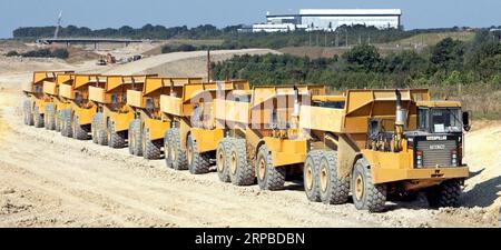 Eine lange Linie von sieben Caterpillar-Dumper-Lkw auf einer neuen Autobahnbaustelle, die eine Verbindungsstraße zum Flughafen Stansted in der Nähe von Takeley in Essex England bilden soll Stockfoto