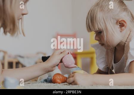 Nahaufnahme von weiblichen Kindern, die mit farbenfrohem Spielzeug in der Küche spielen, Teeset spielen. Kinder liegen auf Teppich zu Hause Schlafzimmer, Kindergarten. Umweltfreundliche Lernspiele. Entwicklung motorischer Fähigkeiten, Phantasie Stockfoto