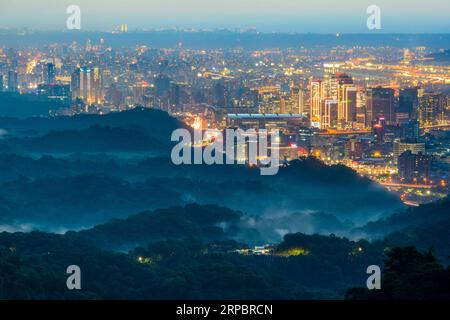 Stadtlichter und wechselnde Wolken: Ein Spektakel, das von der Spitze eines Berges aus gesehen wird. Blick auf die Stadtlandschaft vom Dajianshan Mountain, New Taipei City, Stockfoto