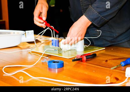 Ein Mann, der Elektriker arbeitet, sammelt den Stromkreis einer großen weißen Straßenlaterne mit Drähten, ein Relais in einer Fabrik eines Industriewerkes. Stockfoto
