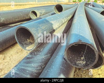 Bau einer Kanalisation in einem neuen Mikrobezirk. Schwarze Gummirohre liegen auf der Baustelle auf dem Sand. Abflusssystem. Stockfoto