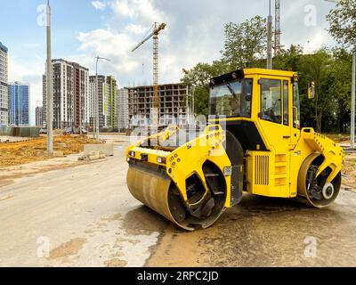 Bau neuer Gebäude und Bauten, hoher Häuser für das Leben der Menschen. Straßenbau auf Asphalt. Gelbes Auto verdichtet Beton. Asphaltfertiger A Stockfoto