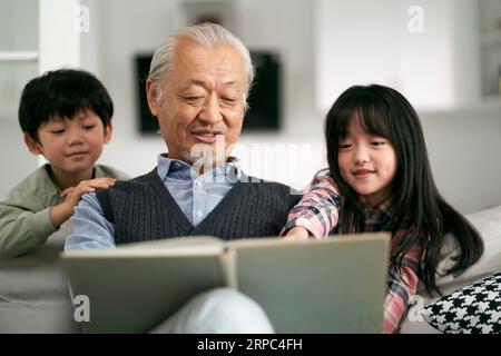 Seniorengroßvater aus Asien hat sich mit zwei Enkeln zu Hause amüsiert Stockfoto