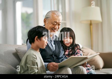 asiatischer Großvater hat Spaß dabei, dem süßen Enkel und der süßen Enkelin eine Geschichte zu erzählen Stockfoto