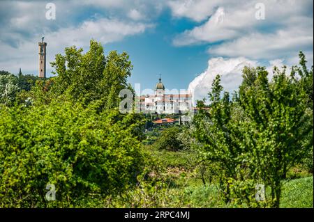 Panoramablick auf die Kirche des Heiligen Andreas mit dem hoch aufragenden Glockenturm, gekrönt von einem Engel, in der Stadt Trissino, Italien Stockfoto