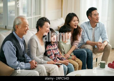 Eine asiatische Familie der 3. Generation, die zu Hause auf der Couch sitzt und zusammen fernsieht, glücklich und lächelnd Stockfoto