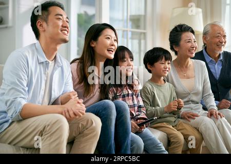 Eine asiatische Familie der 3. Generation, die zu Hause auf der Couch sitzt und zusammen fernsieht, glücklich und lächelnd Stockfoto