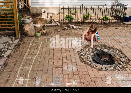 Kleines Mädchen in Armform zieht sich auf die Terrasse im Hinterhof mit Kreide auf dem Bürgersteig Stockfoto